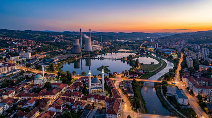 Obraz premium Aerial view of a city with a power plant and a river at sunset, showcasing urban development and industrial infrastructure.