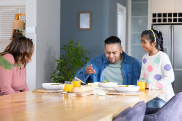 Family with parents and child sharing breakfast at wooden dining table, orange juice, tasting food © wavebreak3