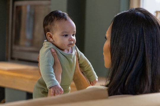 Caregiver lifting baby in green ribbed one-piece to chest, holding under arms, fostering bonding