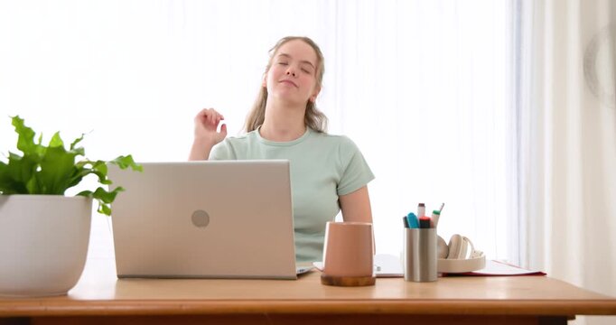 Adult woman in mint T-shirt stretching, relieving tension, then returning to laptop typing at desk