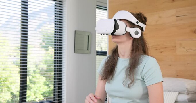 Woman reaching for white VR headset by phone on bed, adjusting and selecting virtual menus