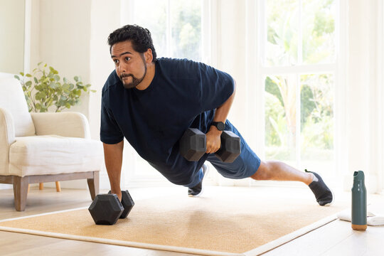 Mid-adult African American man performing hex dumbbell row on natural-fiber rug in living room