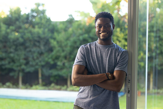 African American man leaning at sliding glass door, smiling toward camera, showing pool, copy space