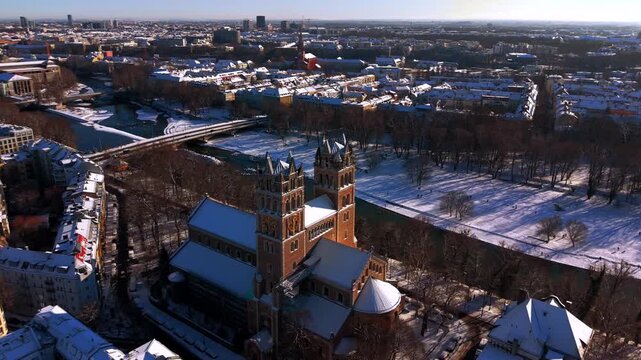 Munich city skyline in winter featuring the Isar River, Reichenbach Bridge, and St. Maximilian church. Beautiful snowy landscape in the capital of Bavaria, Germany.