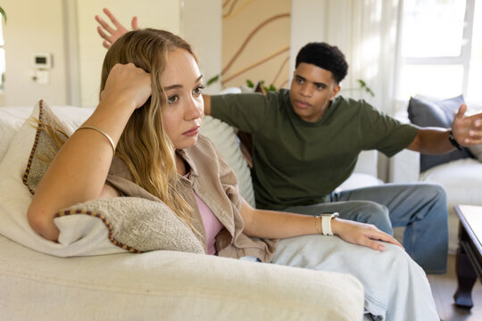Couple having tense conversation on living room sofa amid throw pillows and coffee table