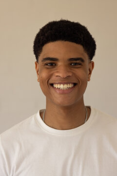 African American man smiling in white crewneck T-shirt wearing silver necklace against beige wall