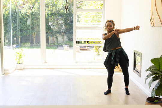 Adult African American woman stretching at home wearing plaid shirt tied by glass doors, copy space