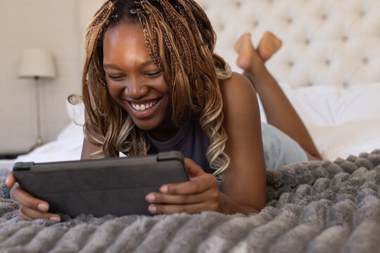 Adult African American woman lying on stomach on bed at home holding tablet in protective case