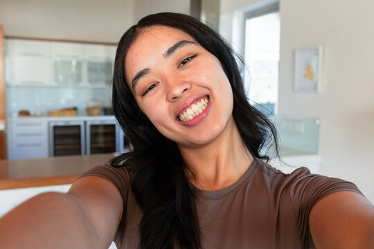 African American woman holding smartphone, smiling and leaning at home in brown top by wine coolers