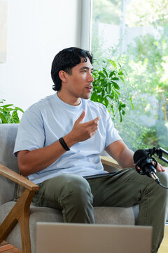 African American man speaking into condenser microphone while gesturing in bright living room