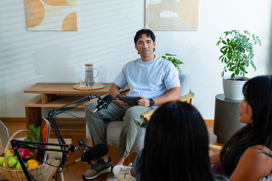 Diverse content creators recording conversation in living room home studio with microphones, tablet