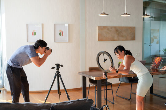 Creators preparing DSLR while female in sportswear adjusting ring light at dining table, copy space