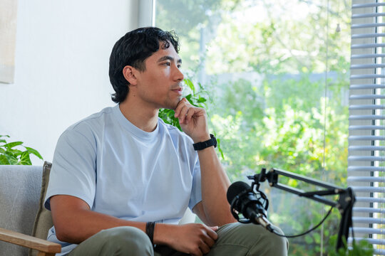 African American man sitting in armchair at home recording podcast with microphone and smartwatch
