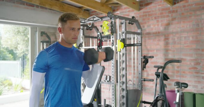 Man gripping pair of hex dumbbells, performing right-arm bicep curls, training strength in home gym