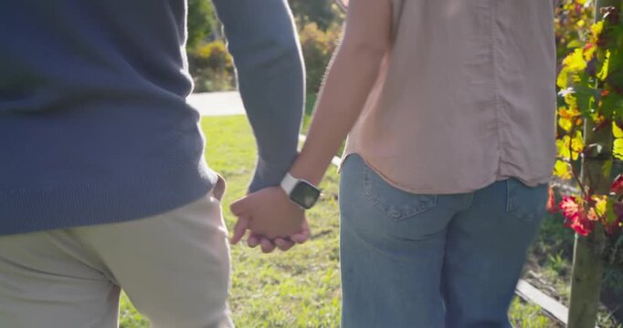 Diverse couple leaving grassy verge for garden path, holding hands with woman's smartwatch visible