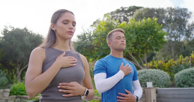 Fitness pair in sportswear following cue, hands on chest and belly, breathing in garden, smartwatch
