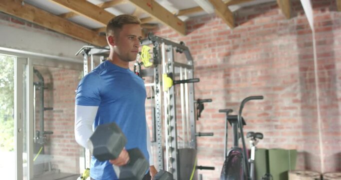 Man curling hex dumbbell in home gym to build strength, camera shifting front to side