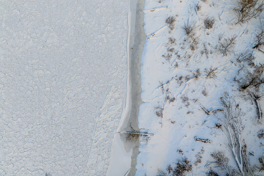 Aerial view of a frozen river with pancake ice floes and a snow-covered bank with bare trees Lithuania.