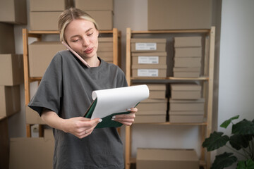 woman making phone call holding clipboard for logistics at startup do inventory. e-commerce and...