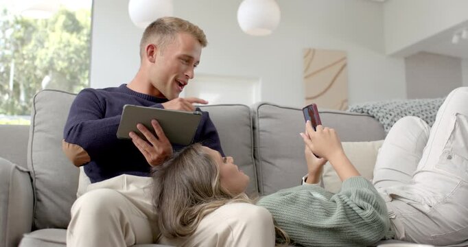 Couple reclining on gray sofa woman tapping phone showing content man leaning and pointing tablet
