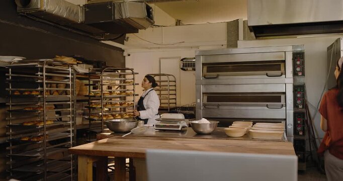 Diverse female staff reviewing laptop walking to prep table consulting tablet chef checking trays