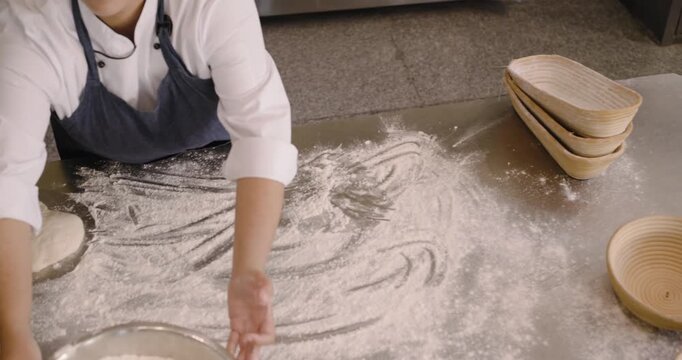 African American woman in apron walking with bowl baskets dusting shaping dough for proof in bakery
