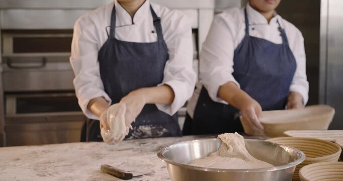 Diverse female bakers scraping dough from bowl, cutting rounds on dusty bench into baskets to proof