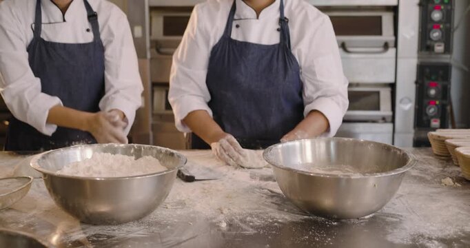 Diverse female bakers in chef coats scooping flour, kneading dough into proofing baskets at bakery