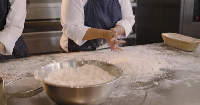 Diverse female bakers in aprons at prep table, dough spurring dusting cutting shaping for proofing