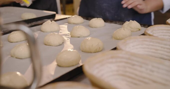 Diverse female bakers aproned tapping, scoring dough on tray at bakery with yellow tool for oven