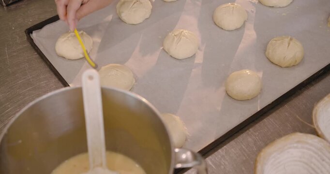 Diverse female bakers dipping yellow brush into bowl, brushing rounds and shaping at bench for oven