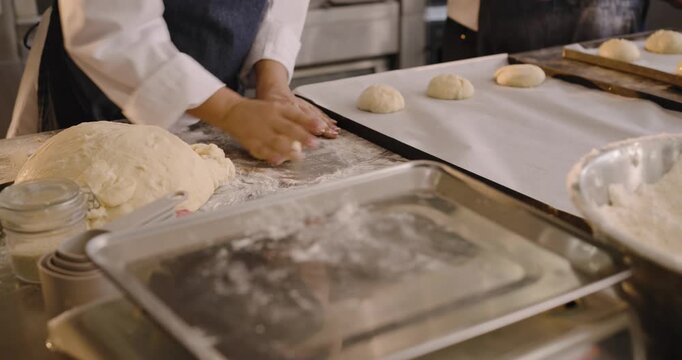 Diverse female bakers in chef coats portioning dough as scale reading guiding rolling to bake