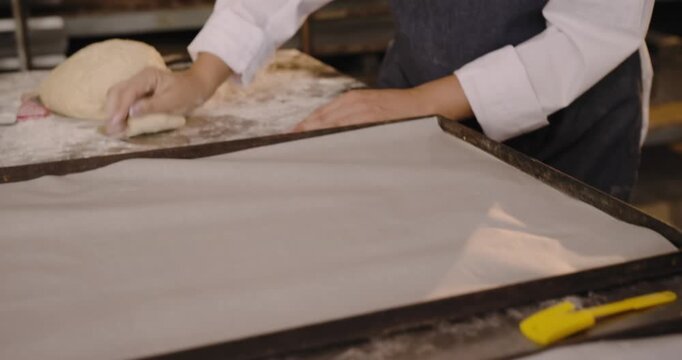 Bakers are pulling pieces from dough and shaping rounds on floured bench, glazing for proofing