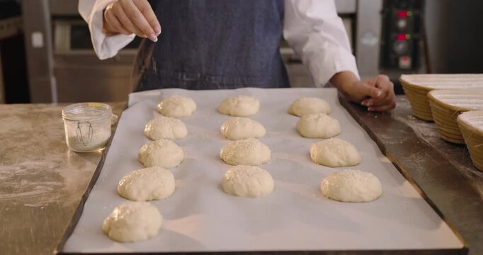 Mid-adult female baker in chef coat dipping jar tapping wash over proofed dough preparing for oven