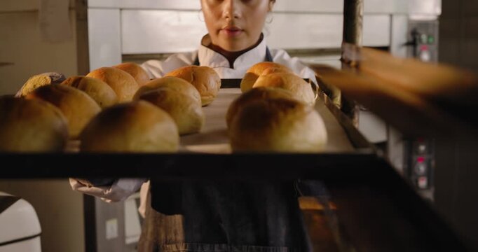 Noticing empty rack African American woman baker in chef coat placing rolls on rack checking color