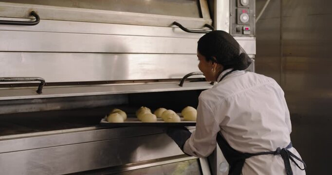 Female baker gloved opening lower deck oven, pulling roll tray, shelving rack to cool, copy space