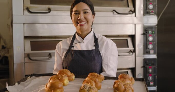 Female baker pulling tray from deck oven checking braided rolls and showing tray to camera smiling