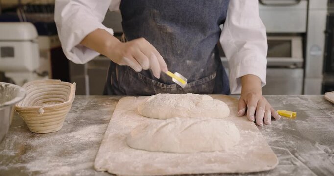 After proofing woman at bakery brushing flour from two loaves with yellow brush preparing for oven