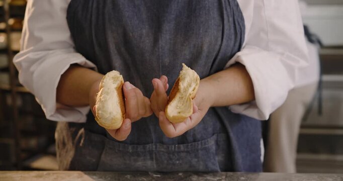 Woman baker holding, pressing, splitting loaf, smelling, tasting, checking crumb at bakery bench