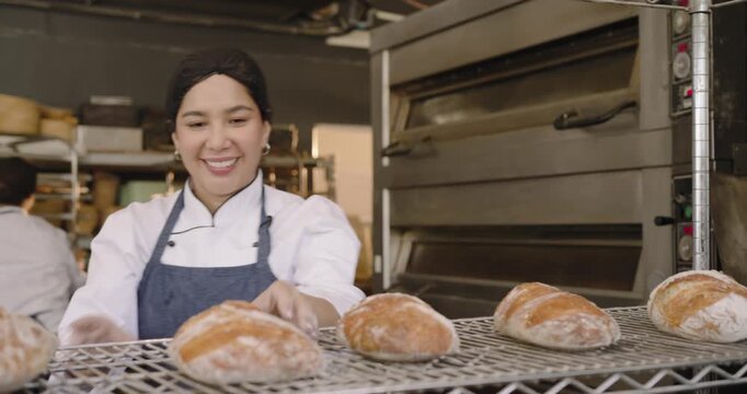 Mid-adult female baker in jacket in bakery after cooling loaves, sorting bread and preparing dough