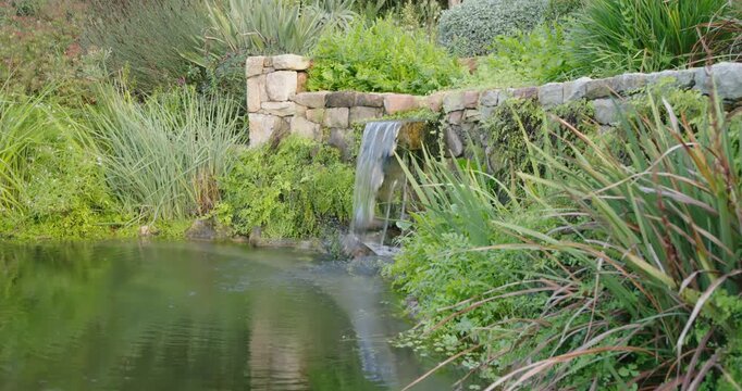 Stone spillway water is issuing from stone lip into pond, creating ripples and downstream flow