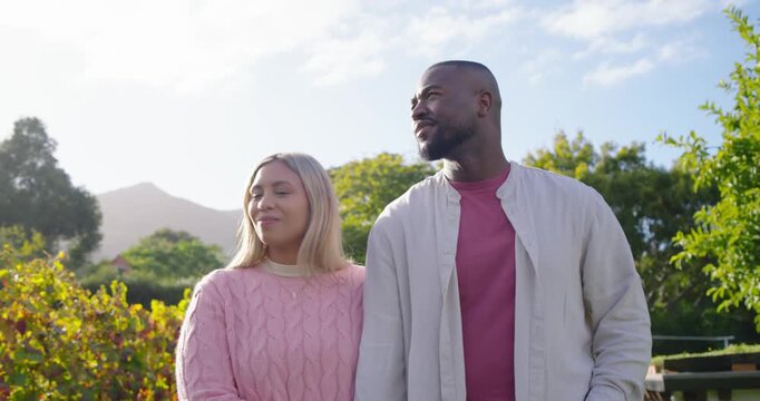 African American couple linking arms walking in garden among shrubs smiling and appreciating view