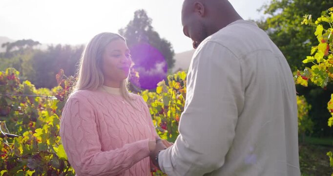 African American couple holding hands in vines woman in pink sweater sun flare man checking ring