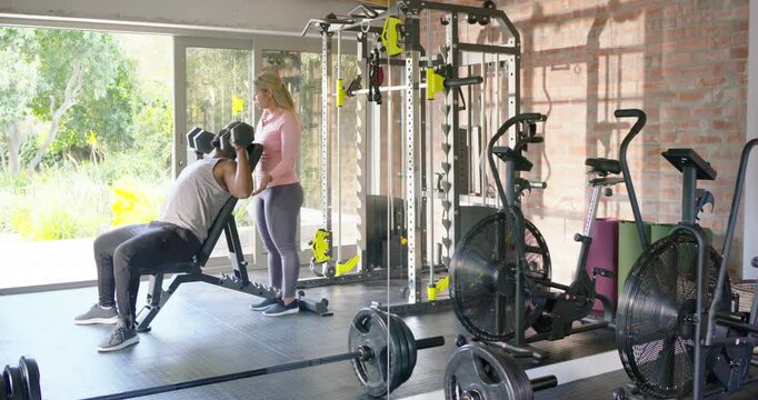 African American trainer spotting man bracing and pressing dumbbells on incline bench for strength