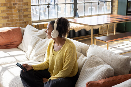 Woman with Headphones Reflecting on Couch with Phone