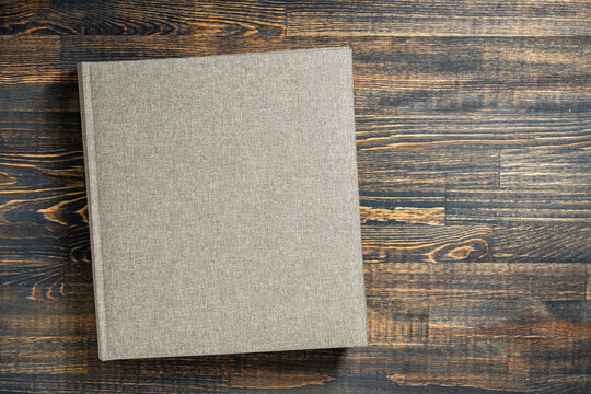 Top view of a grey linen book or photo album on rustic wooden table. Mockup concept for stationery, portfolio, or memory book with copy space