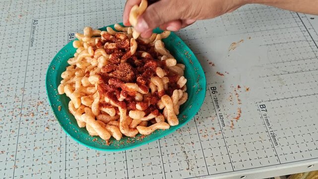 Hand grabbing fried pork rinds with spicy salsa from a plate