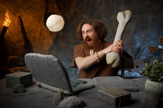 Furious caveman about to smash his stone laptop with a wooden club to solve a computer error.