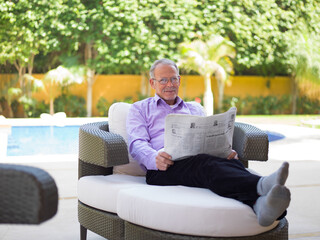 Fototapeta premium Middle Eastern senior man reading newspaper and relaxing at a modern luxury villa by the pool