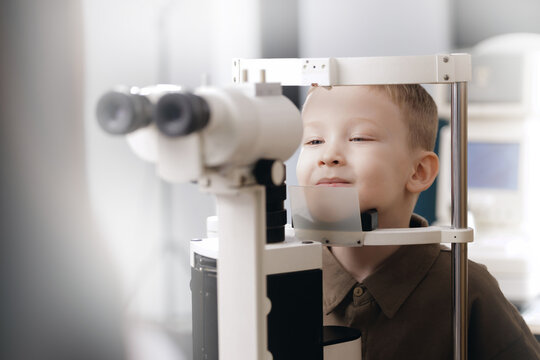 Doctor ophthalmologist and Young boy looking into slit lamp during eye exam clinic